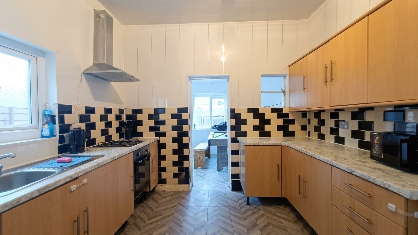 Une cuisine dotée de meubles de rangement en bois, d’un parquet disposé en motif à chevrons et d’une fenêtre laissant entrer la lumière naturelle.