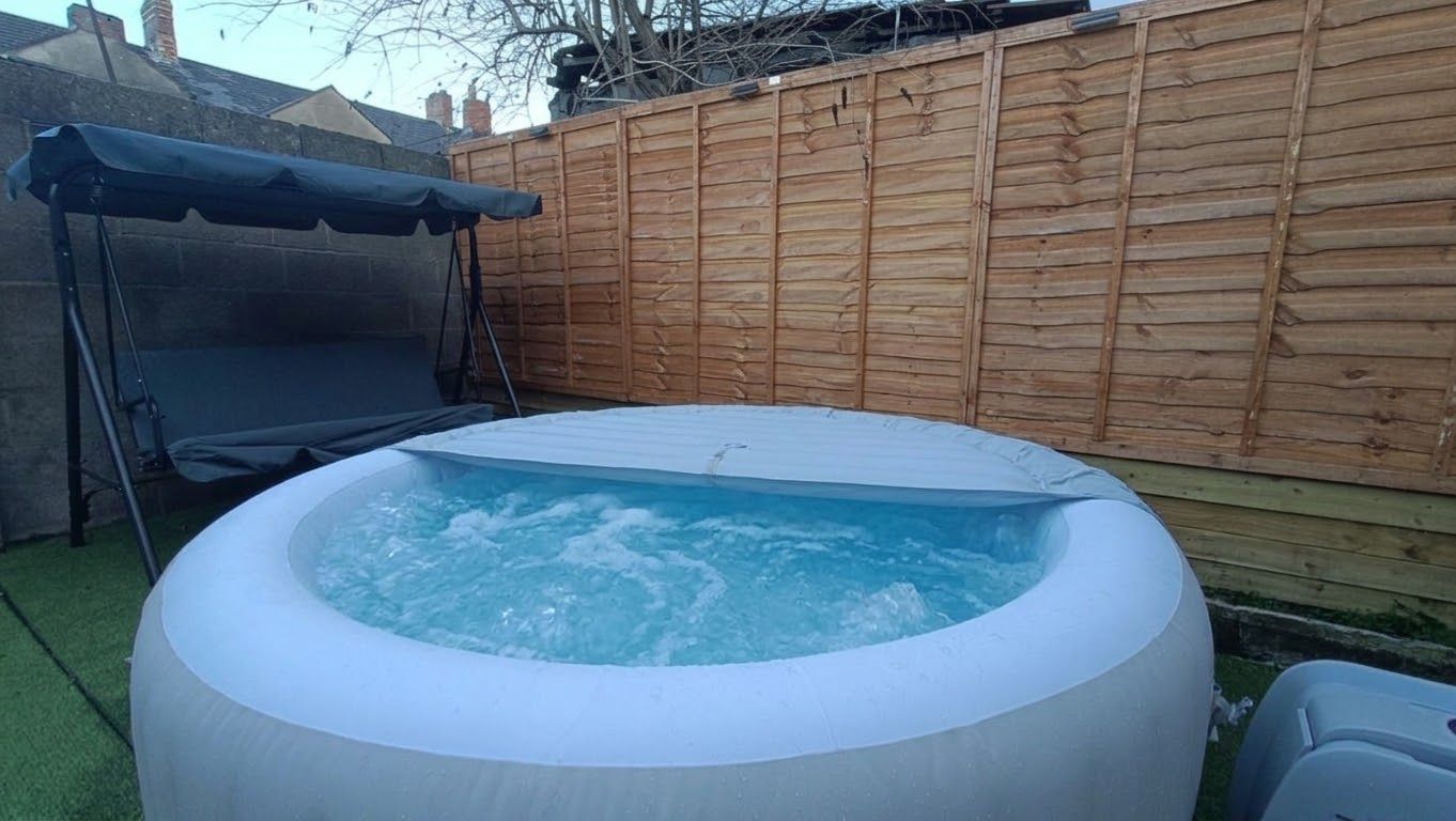 Un jacuzzi dans un jardin, avec une clôture en bois et un trampoline.