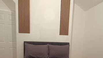 A bedroom with a bed, pillows, and a rolled-up blanket. There are two vertical wooden slats on the wall.