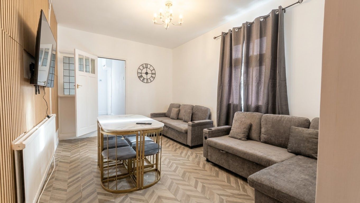Un salon avec un canapé, une petite table, une horloge et un téléviseur fixé au mur.