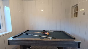 Une table de billard avec des billes et des queues, placée devant un mur blanc à panneaux.