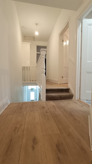 Un hall d’entrée spacieux, doté d’un plancher en bois, d’un escalier et de murs blancs.