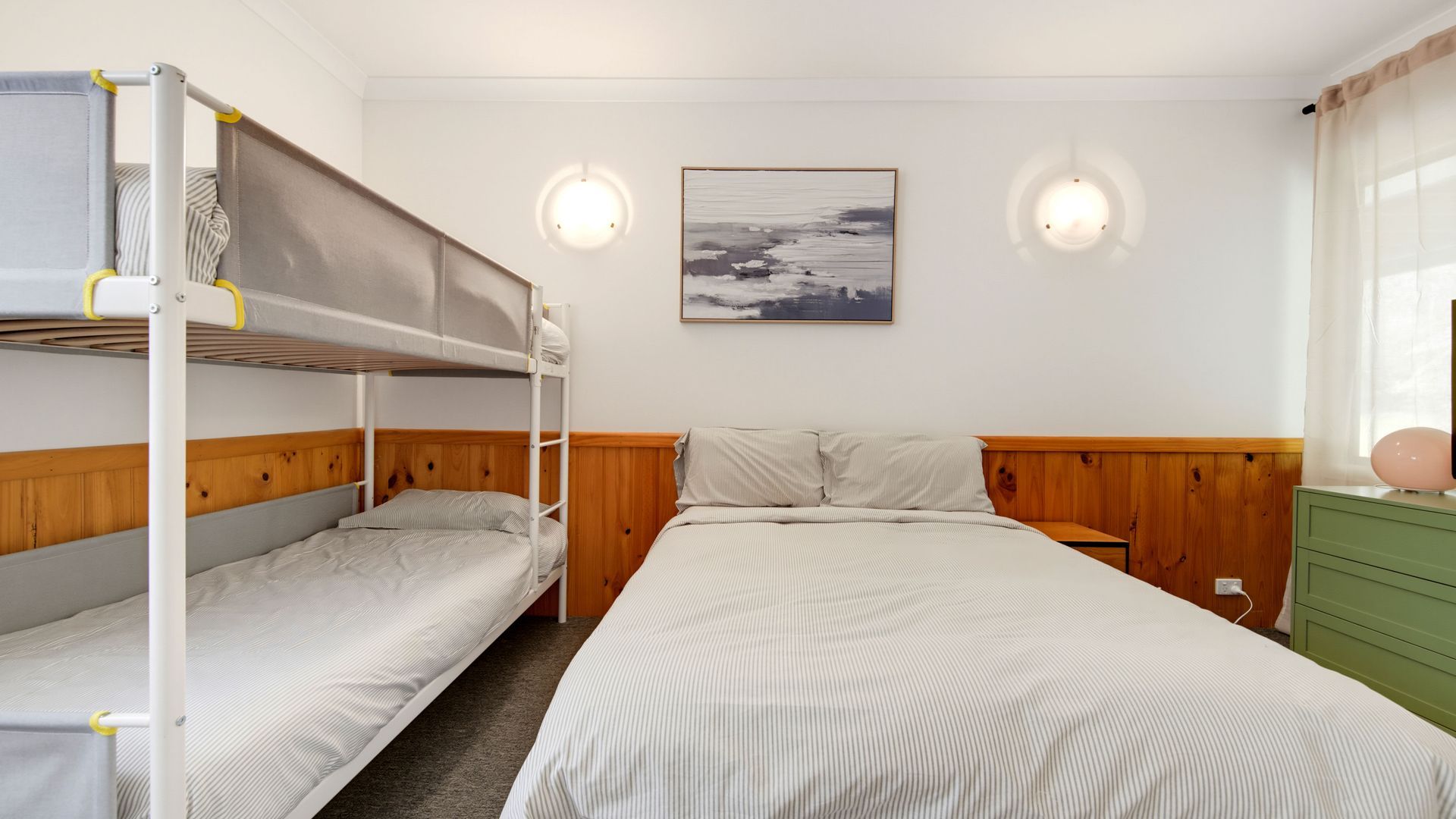 Una habitación con literas, una cama individual, un aparador y dos luces fijadas a la pared.