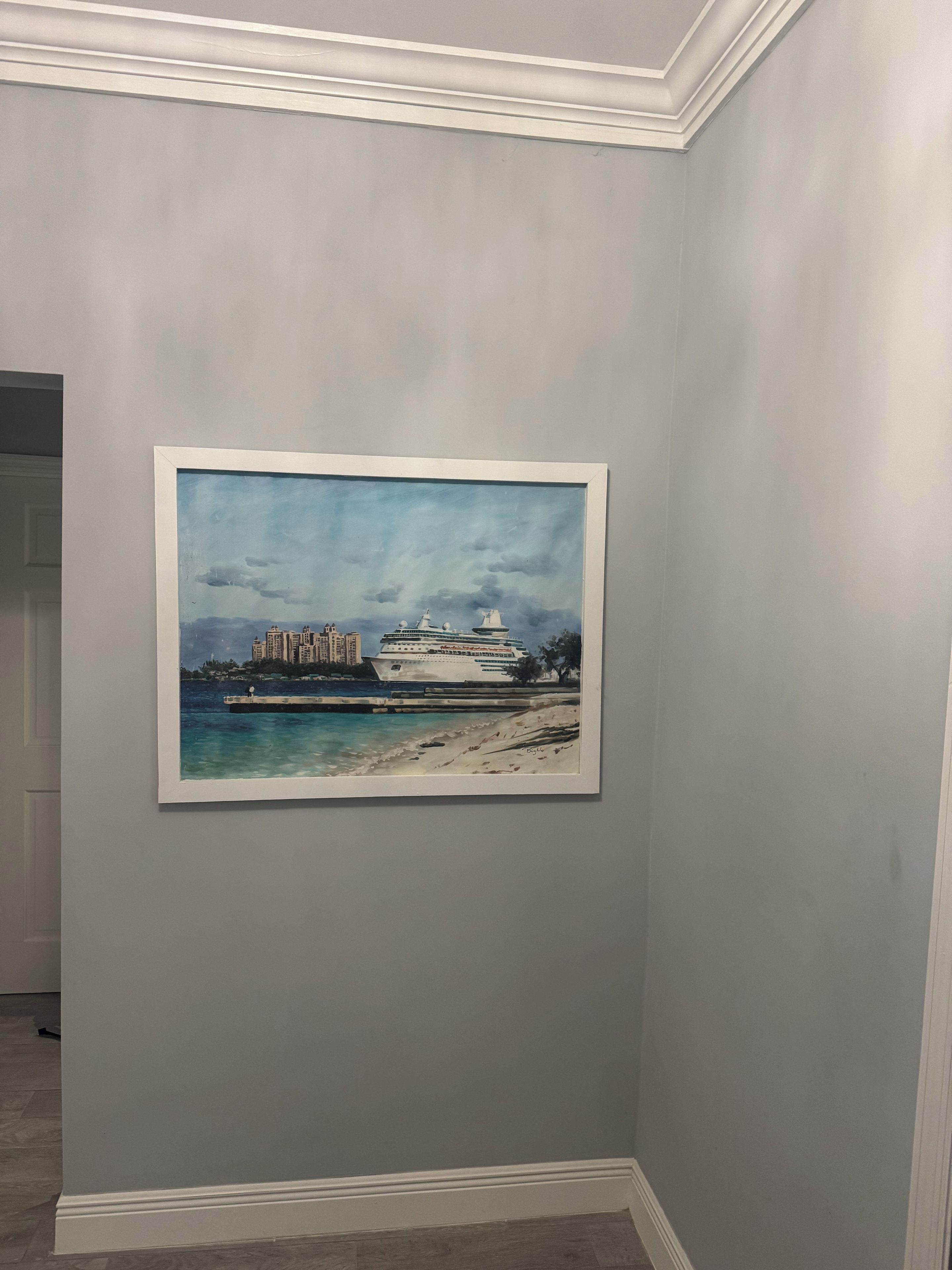Un cuadro enmarco que muestra un crucero en la playa, con edificios al fondo.
