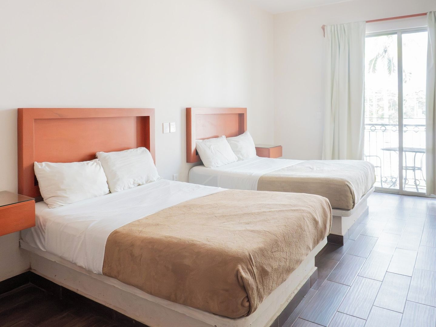 A hotel room with two beds, a balcony, and a view of the outdoors.