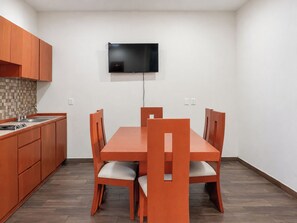 Une cuisine compacte comprenant une table et des chaises, un téléviseur à écran plat fixé au mur et des armoires en bois.