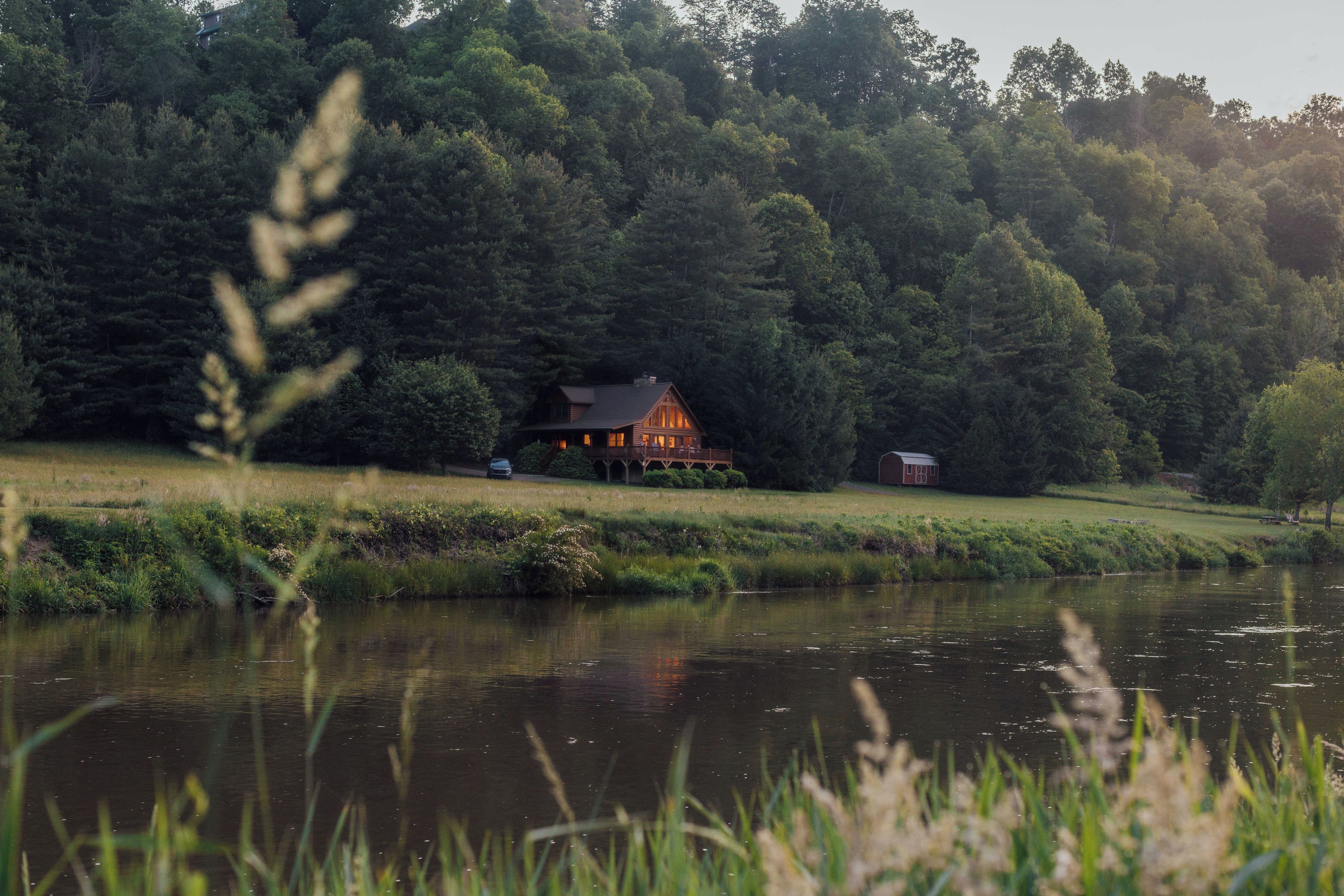 Eine Hütte am See mit einer Terrasse und einem roten Bauernhof im Hintergrund.