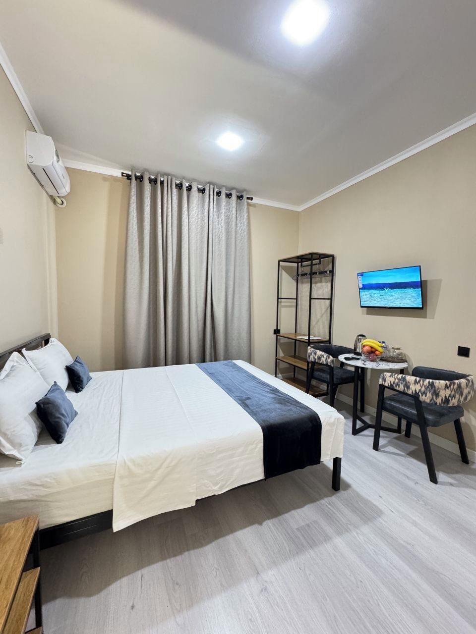 A hotel room with a bed, a TV, a small table with chairs, and a shelf.