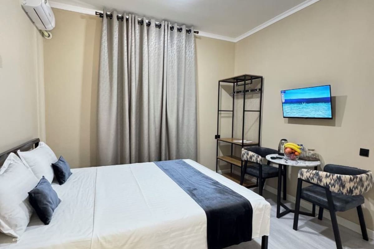 Habitació d'hotel amb un llit, una televisió, una taula petita amb cadires i una estantalia.