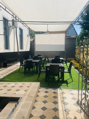 An outdoor seating area with tables and chairs, a projector screen, and a grassy lawn. - LUNA PLAZA HOTEL TASHKENT (Tashkent)
