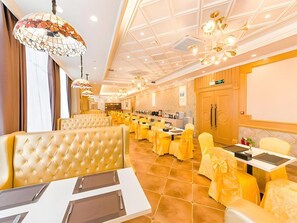 A hotel dining area with multiple tables and chairs, a buffet setup, and a ceiling with decorative lighting fixtures. - Vienna Hotel (Weihai)