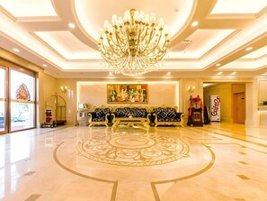 A lobby with a chandelier, sofas, a patterned carpet, and a painting on the wall. - Vienna Hotel (Weihai)