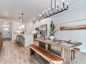 A modern kitchen with white cabinetry, a central island, and a dining area with a wooden bench and table set for six. - Southwestern Home w/ Record Lounge • Family Friendly • 20 Min to OKC & Lazy E (Edmond)
