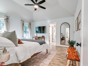 A bedroom with a bed, bedside table, and a desk with a chair. There is a ceiling fan, a TV mounted on the wall, and a large mirror. - Southwestern Home w/ Record Lounge • Family Friendly • 20 Min to OKC & Lazy E (Edmond)