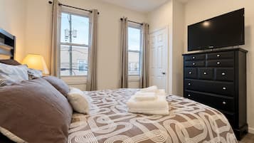 A hotel room with a bed, a dresser, a television, and a window with curtains.