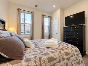 A hotel room with a bed, a dresser, a television, and a window with curtains.