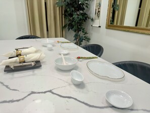 A dining table set with white plates, bowls, and a spoon, with a plant and a mirror in the background.