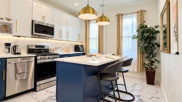 A modern kitchen with white cabinets, a central island, stainless steel appliances, and pendant lighting.