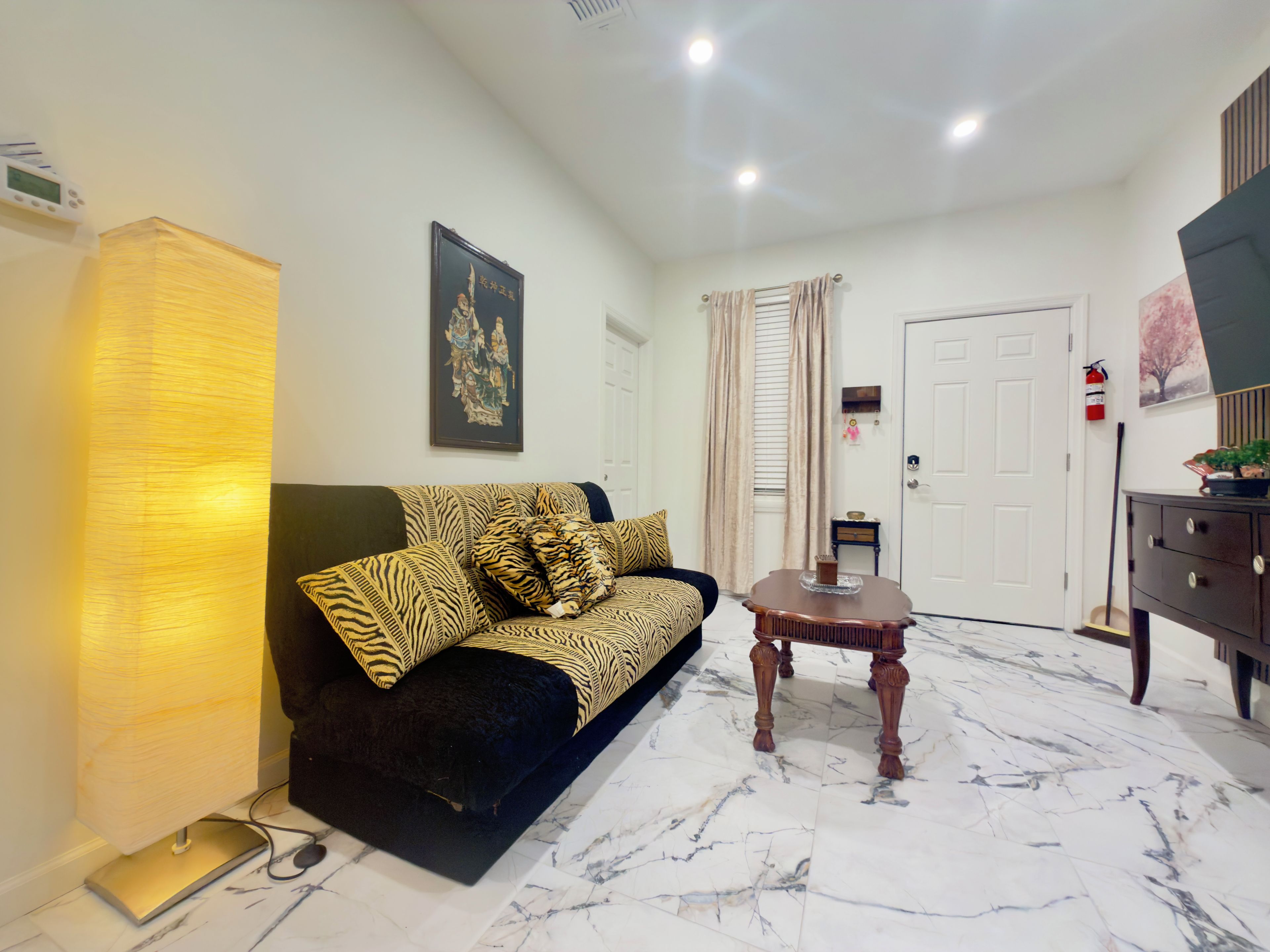 A living room with a sofa, a coffee table, a lamp, a framed picture, a door, and a television.