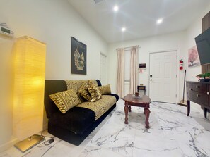 A living room with a sofa, a coffee table, a lamp, a framed picture, a door, and a television.