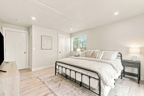 Une chambre à coucher avec un lit, des tables de chevet, une fenêtre avec des stores et une porte.