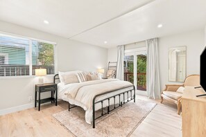 Une chambre à coucher avec un lit, une table de chevet, une lampe et une vue sur la verdure par la fenêtre.