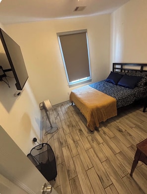 Un dormitorio pequeño con cama, ventana, calefactor y televisor montado en la pared.