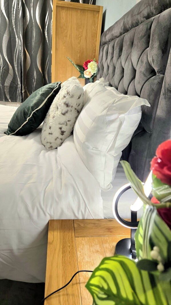 Een bed met witte lakens, een houten hoofdbord en een nachtkastje met een lamp.