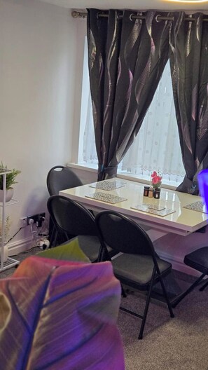 Een kamer met een eettafel, stoelen, een potplant en een raam met gordijnen.