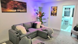 Een woonkamer met een grijze modulaire bank, een vloerlamp en twee ingekaderde foto's aan de muur.