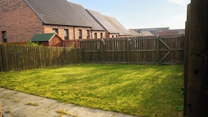 A fenced backyard with a grassy lawn, a brick building with a sloped roof, and a wooden gate. - Bright,modern 4 bedroom house with free Parking (Edinburgh)