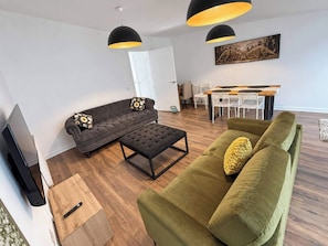 A modern living room with a sofa, ottoman, and a dining area with chairs and a table. - Bright,modern 4 bedroom house with free Parking (Edinburgh)