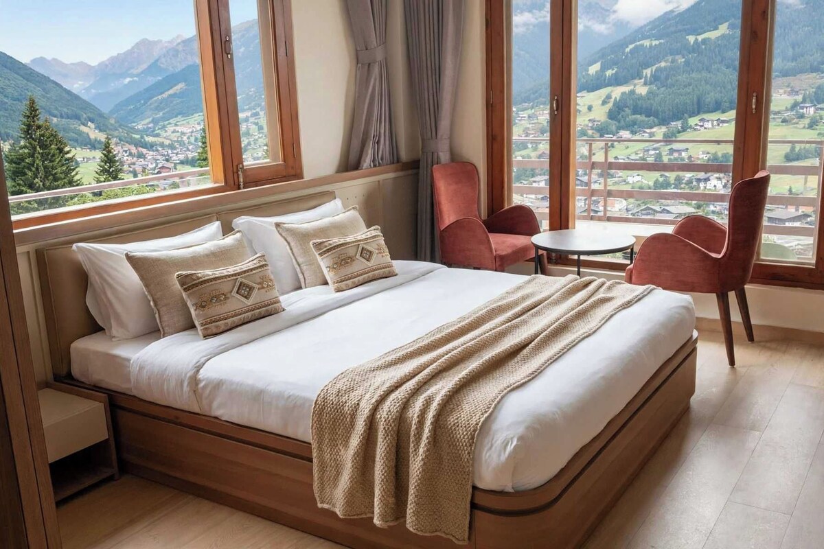 Ein Schlafzimmer mit einem großen Bett, Blick auf Berge, einem kleinen Tisch und zwei Stühlen.