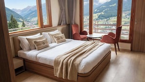 Ein Schlafzimmer mit einem großen Bett, Blick auf Berge, einem kleinen Tisch und zwei Stühlen.