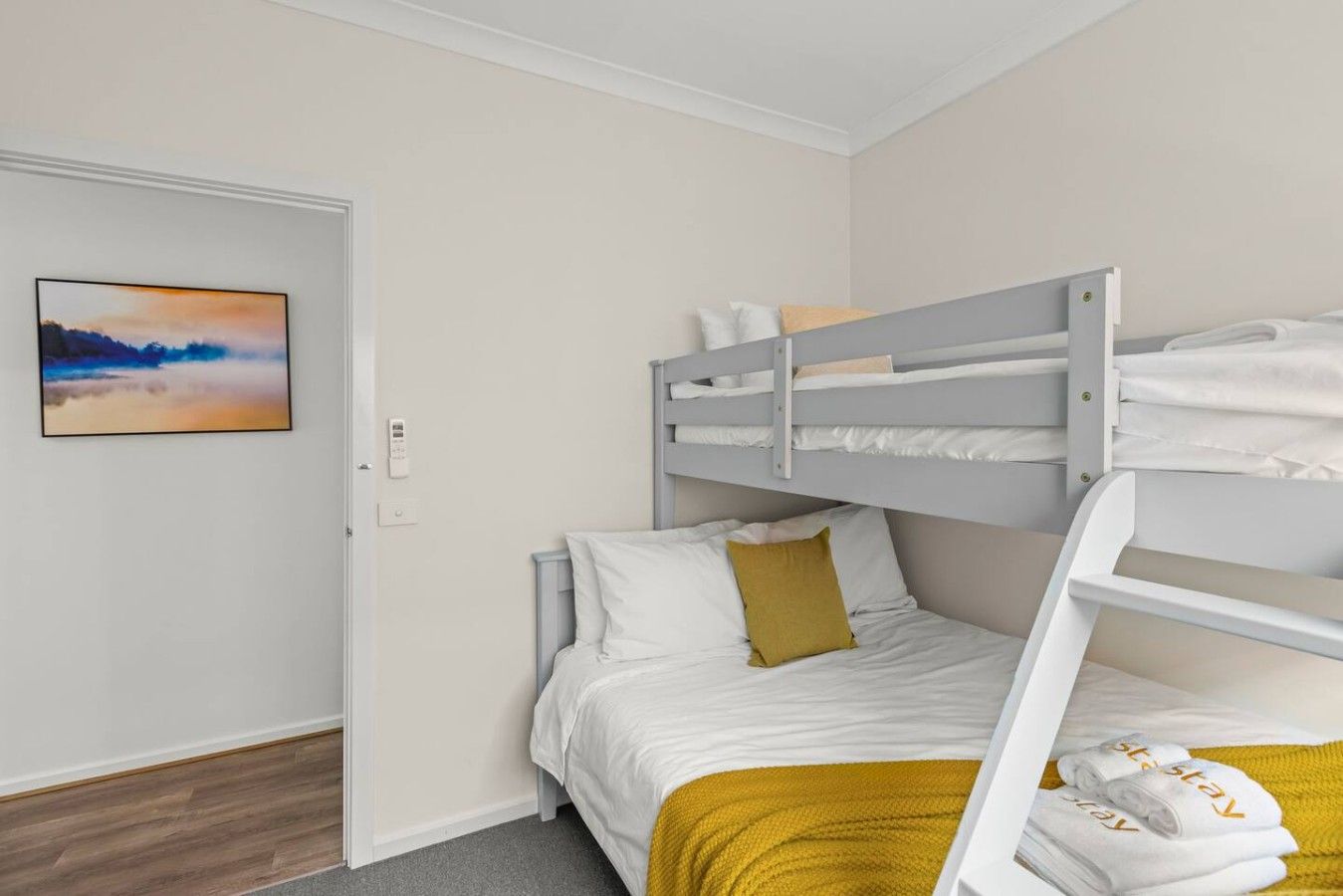 A bunk bed room with a single bed and a bunk above. There is a painting on the wall and a door to the left.