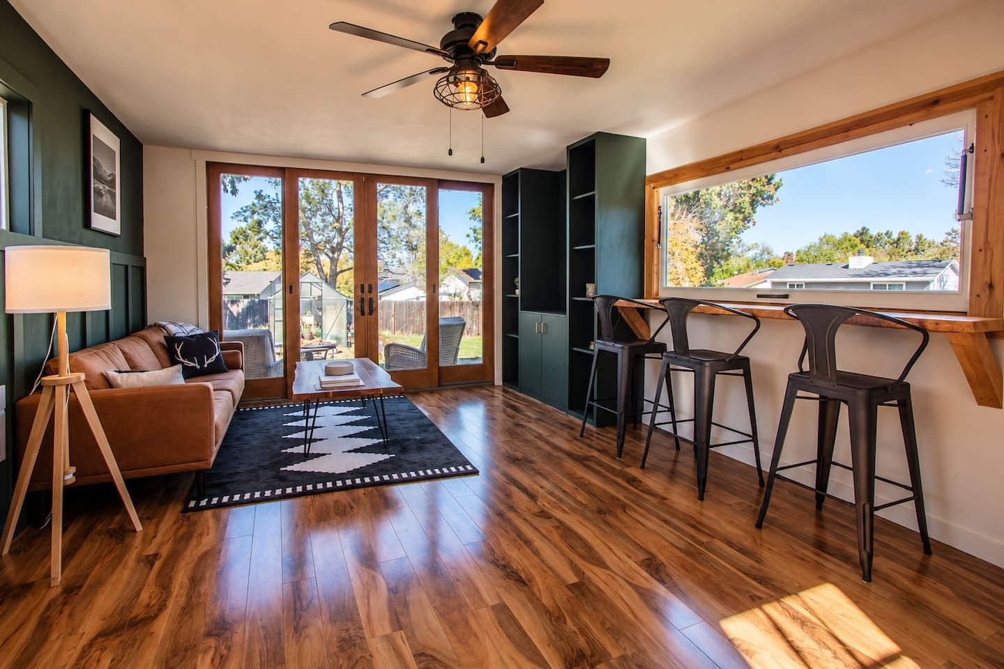 A modern living room with a wooden floor, a ceiling fan, a sofa, a coffee table, and a view through large sliding glass doors.