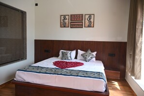 Una cama bien hecha con un arreglo en forma de corazón de flores rojas, un cabecero de madera y tres cuadros en la pared.