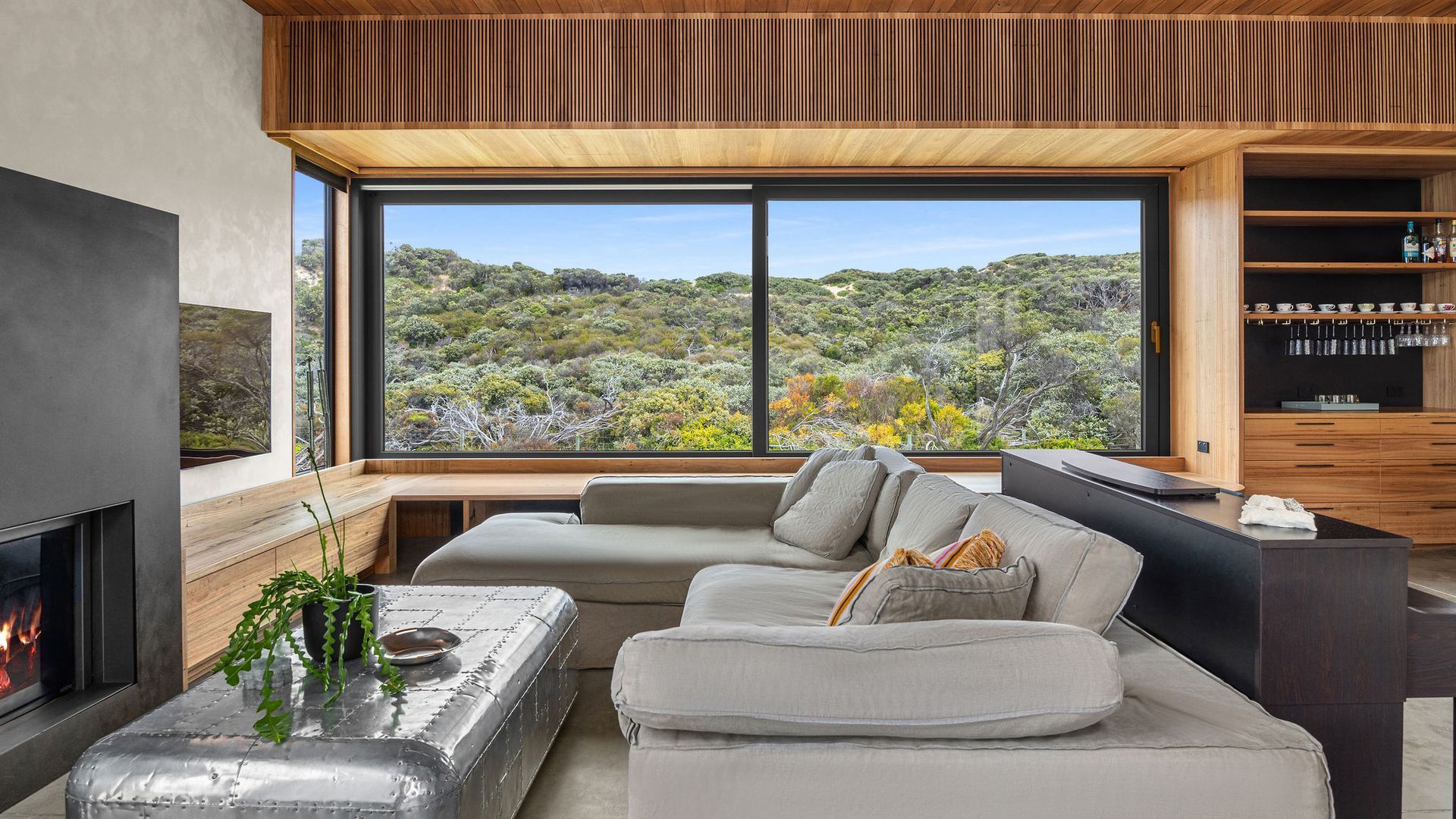 A modern living room with a large window, a fireplace, and a built-in bookshelf.