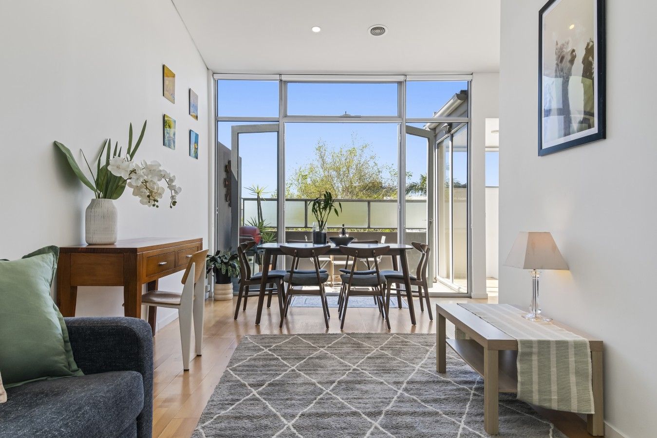 A modern living room with a dining area, large windows, and a view of the outdoors.