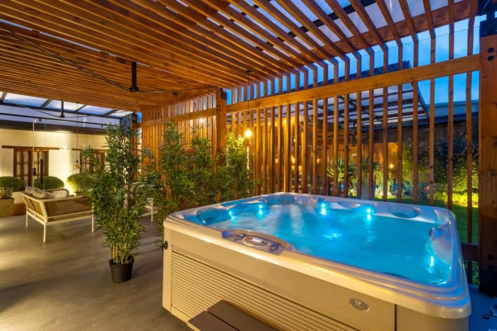 A hot tub in a covered outdoor area with wooden beams and potted plants.