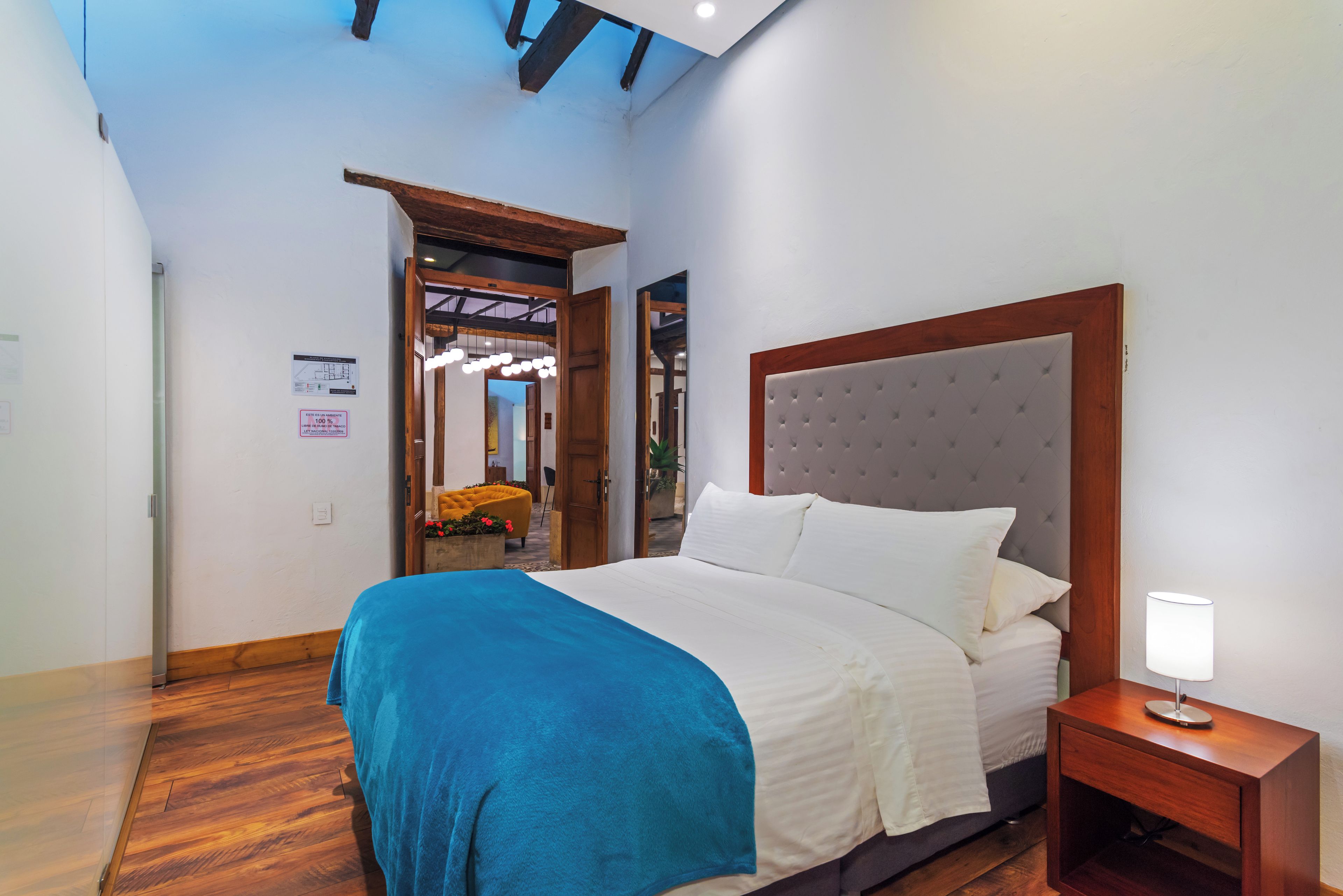 Quarto de hotel com cama, mesa de cabeceira e vista para o corredor.
