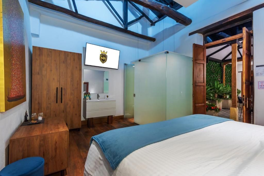 A bedroom with a bed, wooden wardrobe, a mirror, and a television displaying a logo.