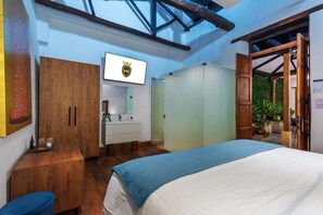 A bedroom with a bed, wooden wardrobe, a mirror, and a television displaying a logo.