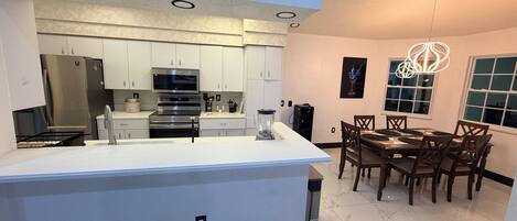 A modern kitchen with a central island, white cabinetry, stainless steel appliances, and a dining area with wooden chairs and a table.
