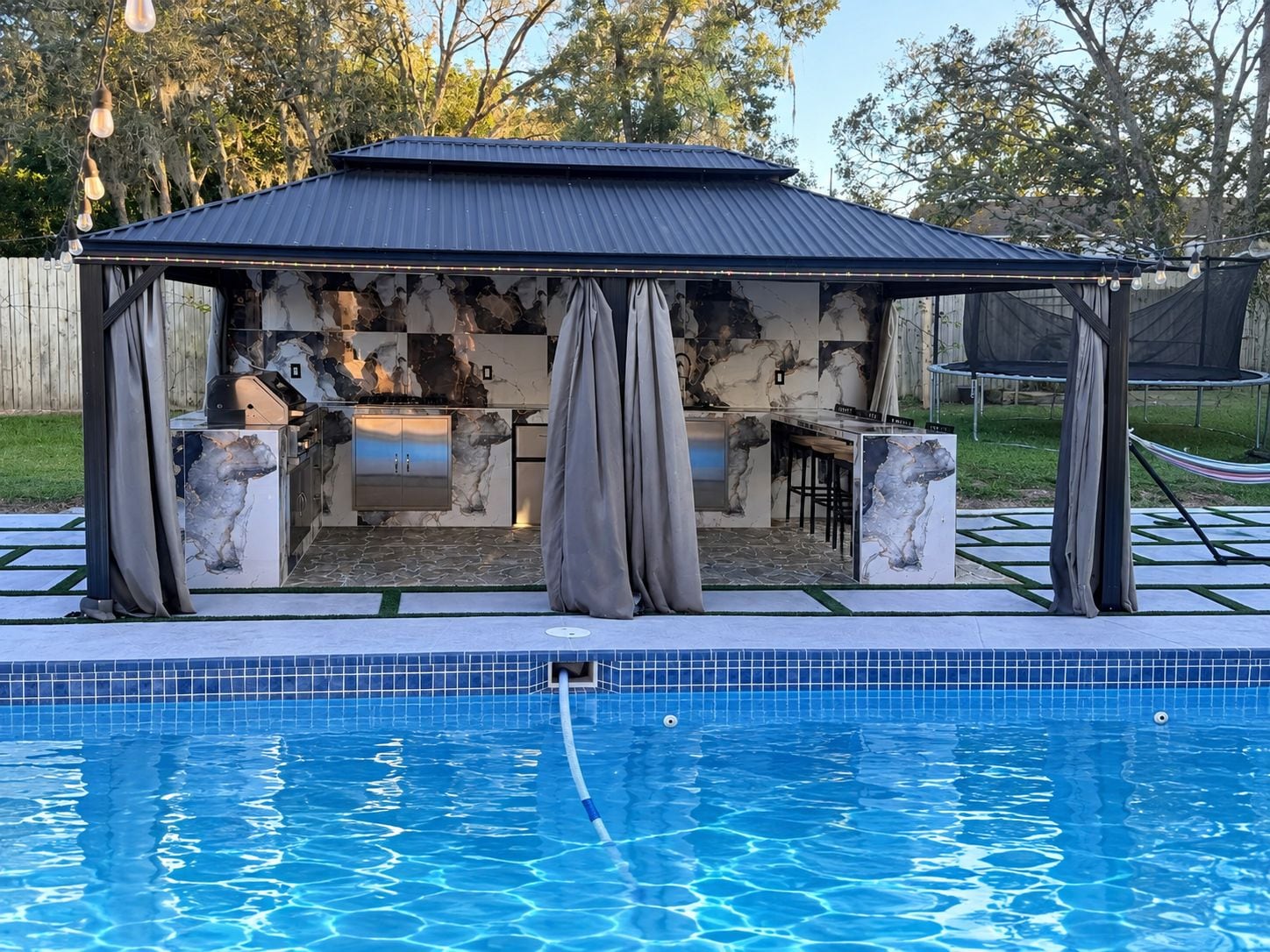 A poolside gazebo with a built-in grill and bar area, surrounded by a swimming pool.