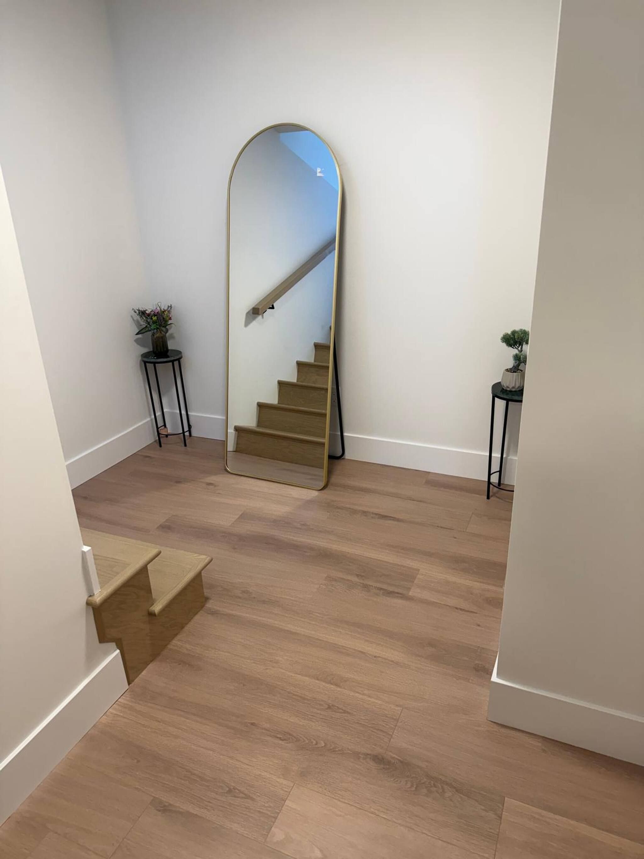 A hallway with a wooden floor, a large mirror, and a staircase.