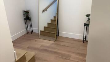 A hallway with a wooden floor, a large mirror, and a staircase.