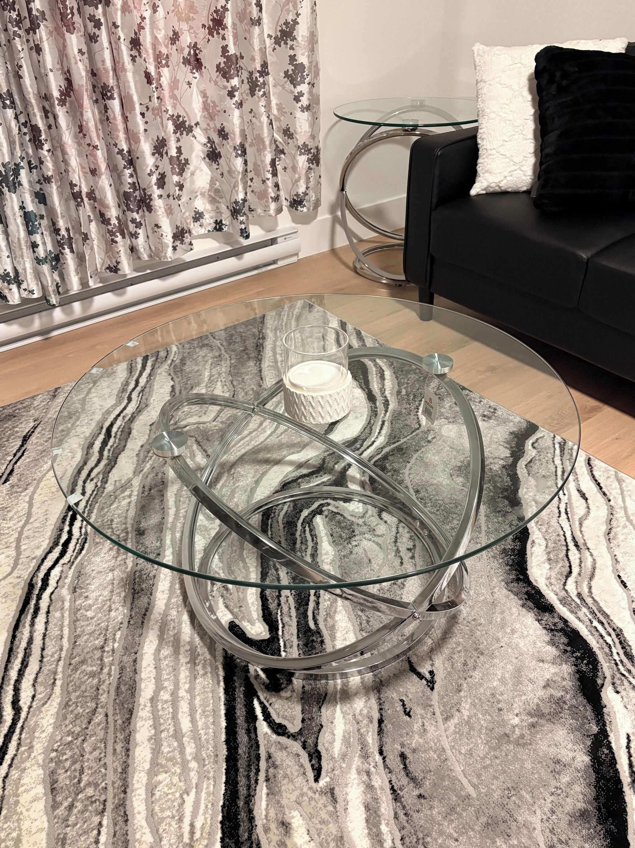 A modern living room with a glass coffee table, a black sofa, and a patterned rug.