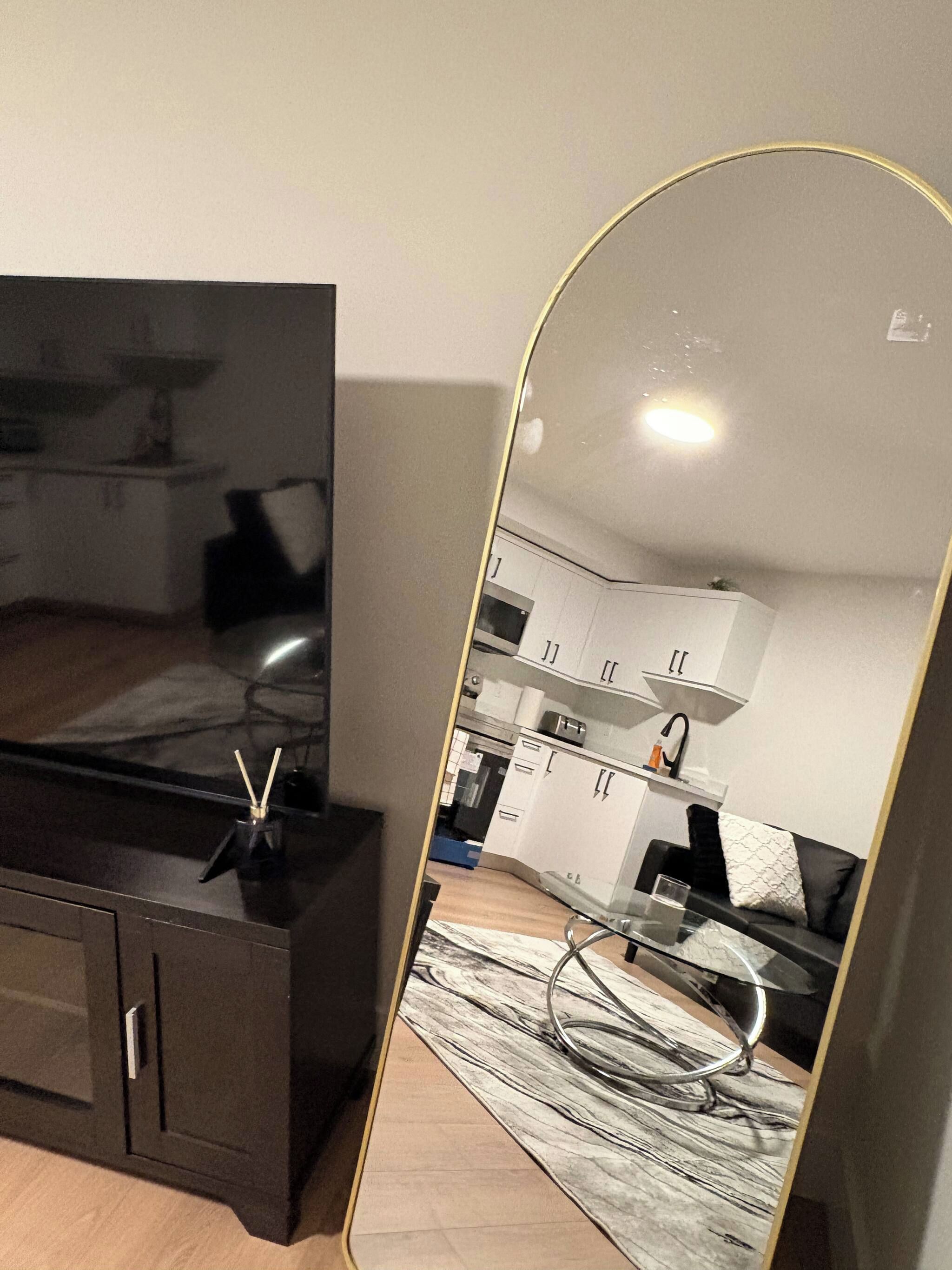 A modern living room with a dark wooden entertainment unit, a large flat-screen TV, and a mirrored wall reflecting the room.