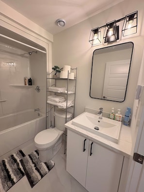 Une salle de bain moderne avec une baignoire, des toilettes et un lavabo. On y trouve un porte-serviettes avec des serviettes pliées et une petite plante.